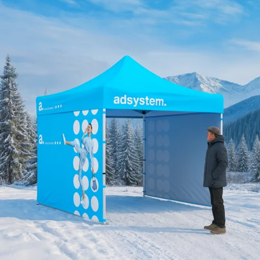 Namiot reklamowy adsystem ustawiony w zimowym krajobrazie gorskim, otoczony sniegiem i osniezonymi drzewami, z mezczyzna stojacym obok konstrukcji.
