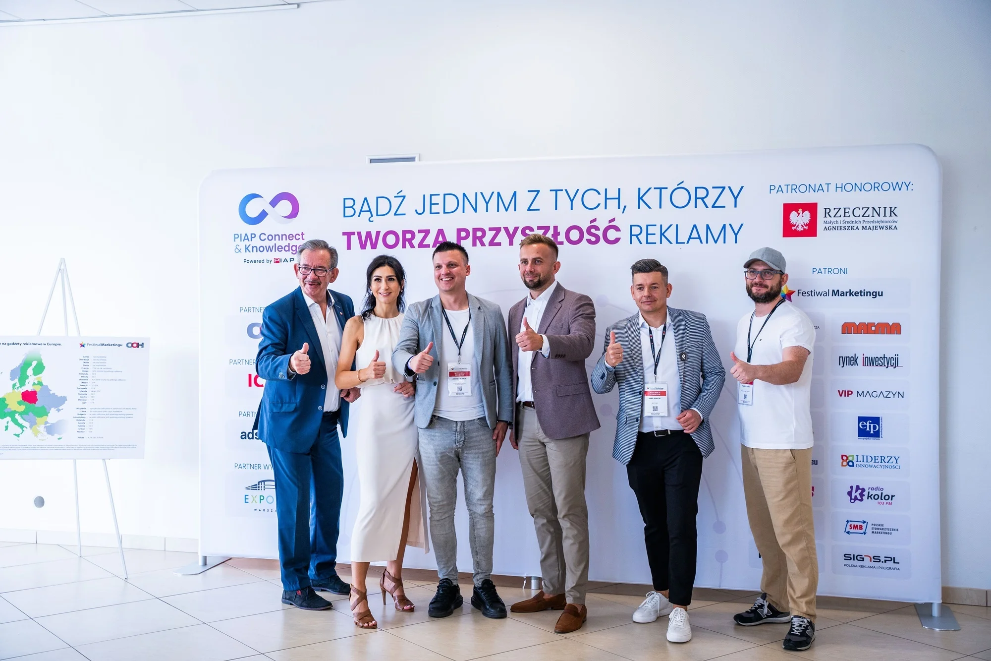 Uczestnicy eventu na tle ścianki reklamowej z logo
