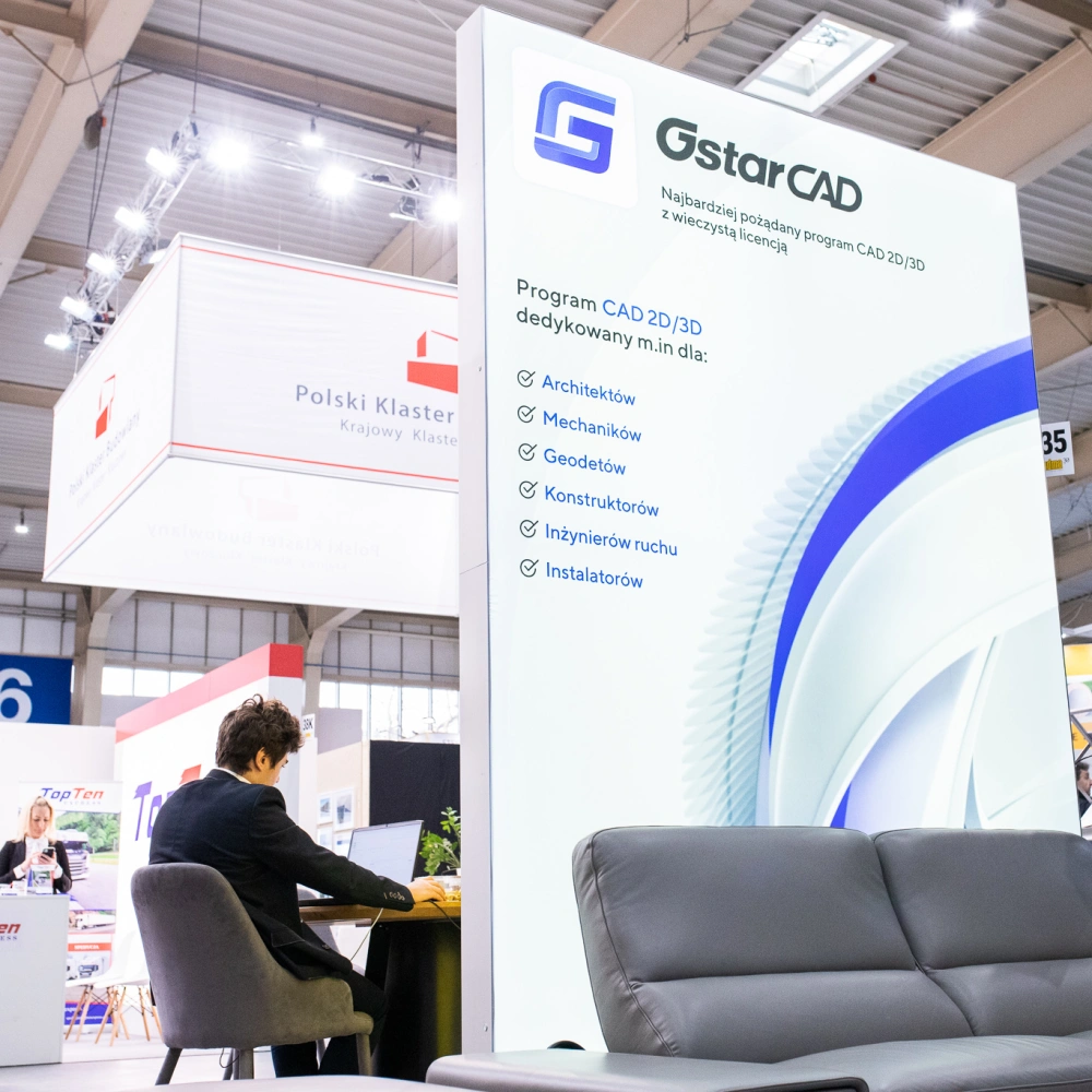 Stoisko targowe z dużą grafiką promującą oprogramowanie CAD 2D/3D, listą branż docelowych, strefą do pracy przy laptopie oraz miejscem wypoczynkowym z sofą.