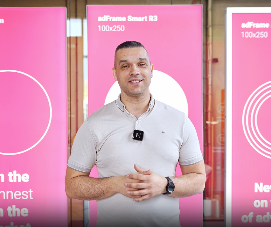 Prezentacja trzech kasetonów reklamowych adFrame Slim, Smart R3 i Lumina RGB o wymiarach 100x250, z osobą prowadzącą stojącą na tle różowych grafik promocyjnych.