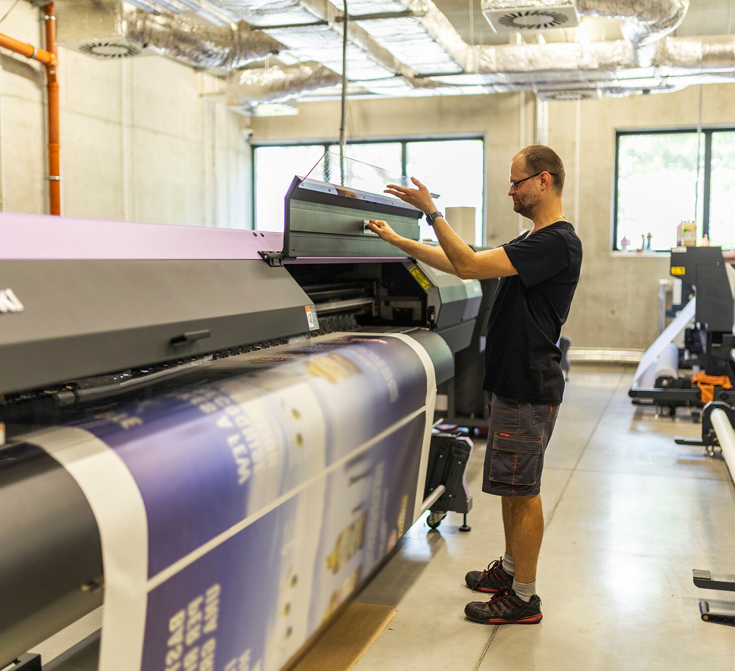 Pracownik obsługujący wielkoformatową drukarkę solwentową w nowoczesnej hali produkcyjnej.