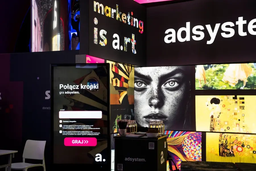 Stoisko na targi adsystem z hasłem „Marketing is art”, interaktywnym ekranem i kolorowymi grafikami.