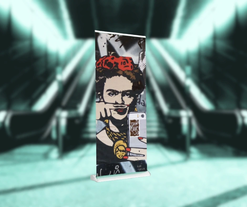 Roll-up z kolorową grafiką w stylu pop-art przedstawiającą kobietę z czerwonym nakryciem głowy, ustawiony na tle rozmytej przestrzeni z ruchomymi schodami w tle.