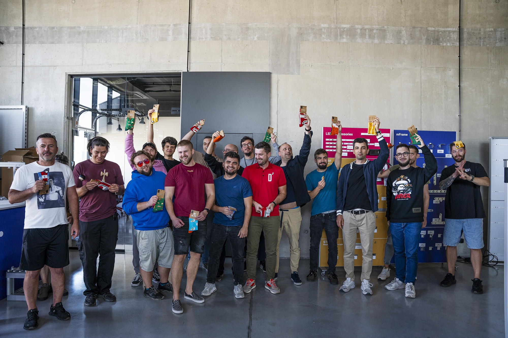 Grupa pracowników pozuje z kolorowymi skarpetkami w rękach – uśmiechnięci uczestnicy firmowej akcji prezentowej w industrialnej przestrzeni biurowej.