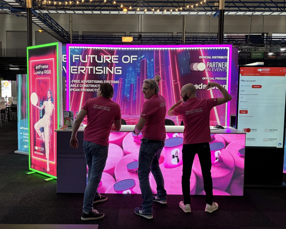 Zespół prezentujący stoisko adsystem z futurystycznym podświetleniem podczas targów, w koszulkach z napisem „The Future of Advertising”.