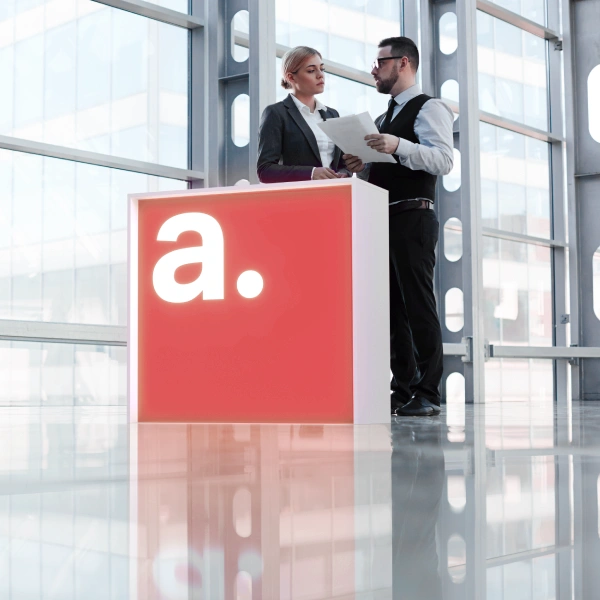 Minimalistyczna trybunka podświetlana z logotypem „a.” w nowoczesnym wnętrzu hali targowej – elegancka forma prezentacji marki.