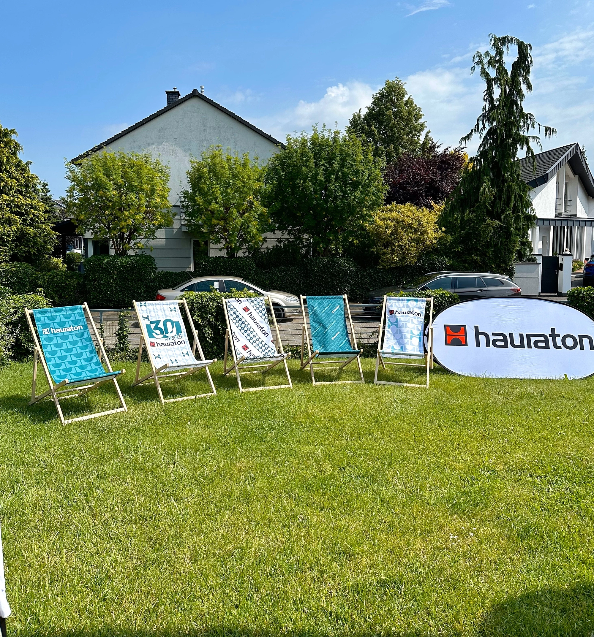 Leżaki reklamowe ustawione na trawie na tle osiedla domów jednorodzinnych