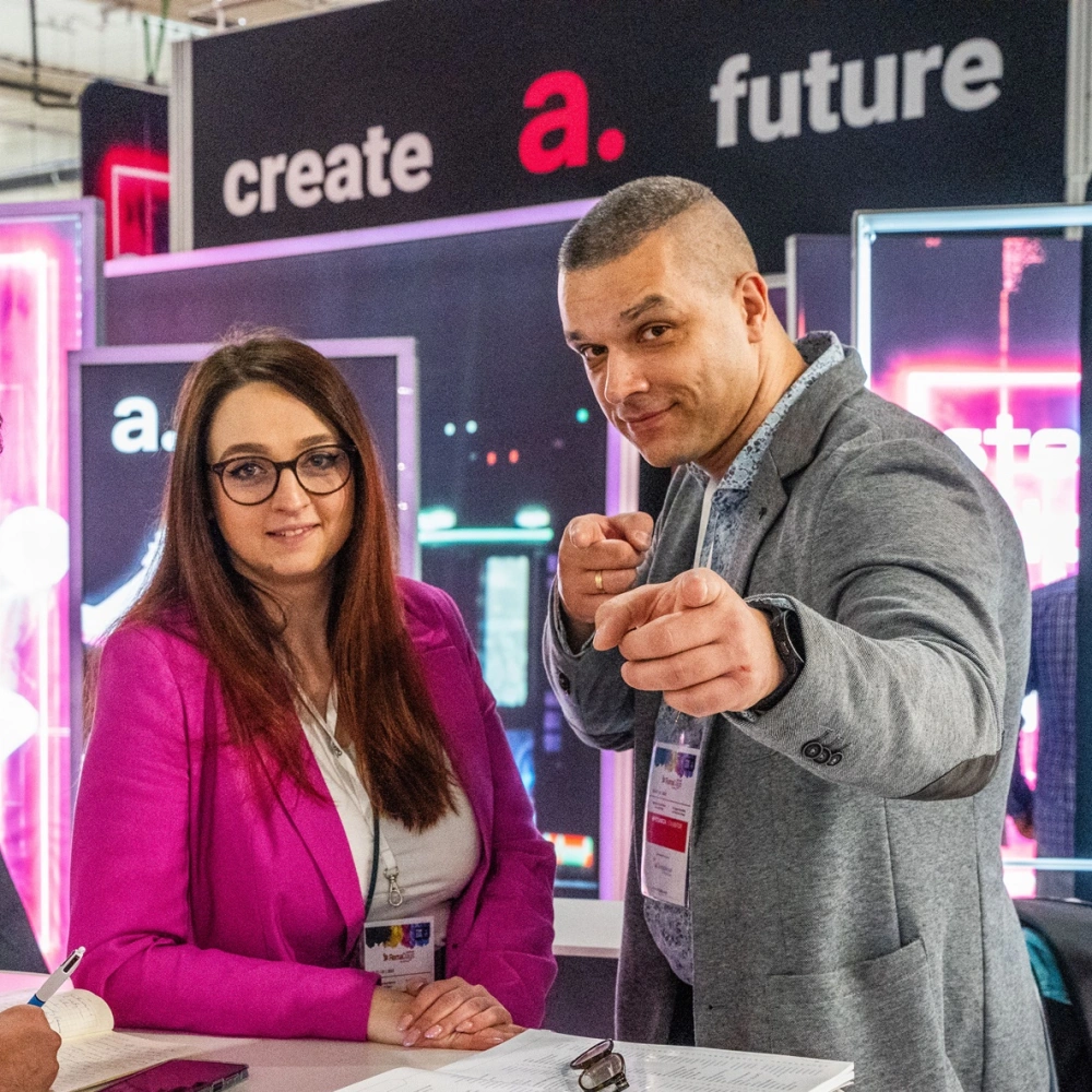 Miembros del equipo de adsystem en una feria, interactuando con entusiasmo frente a un fondo con el eslogan “create a future”.