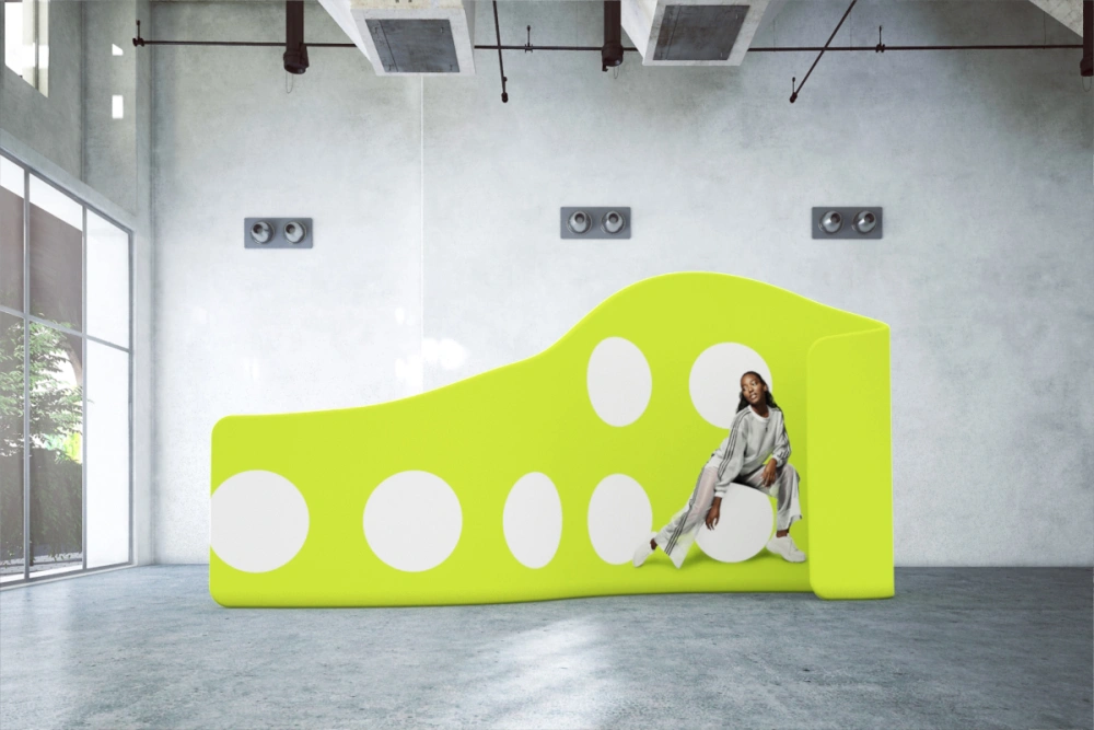 Falowana ścianka tekstylna z nadrukiem w jaskrawej kolorystyce, ustawiona w industrialnym wnętrzu.