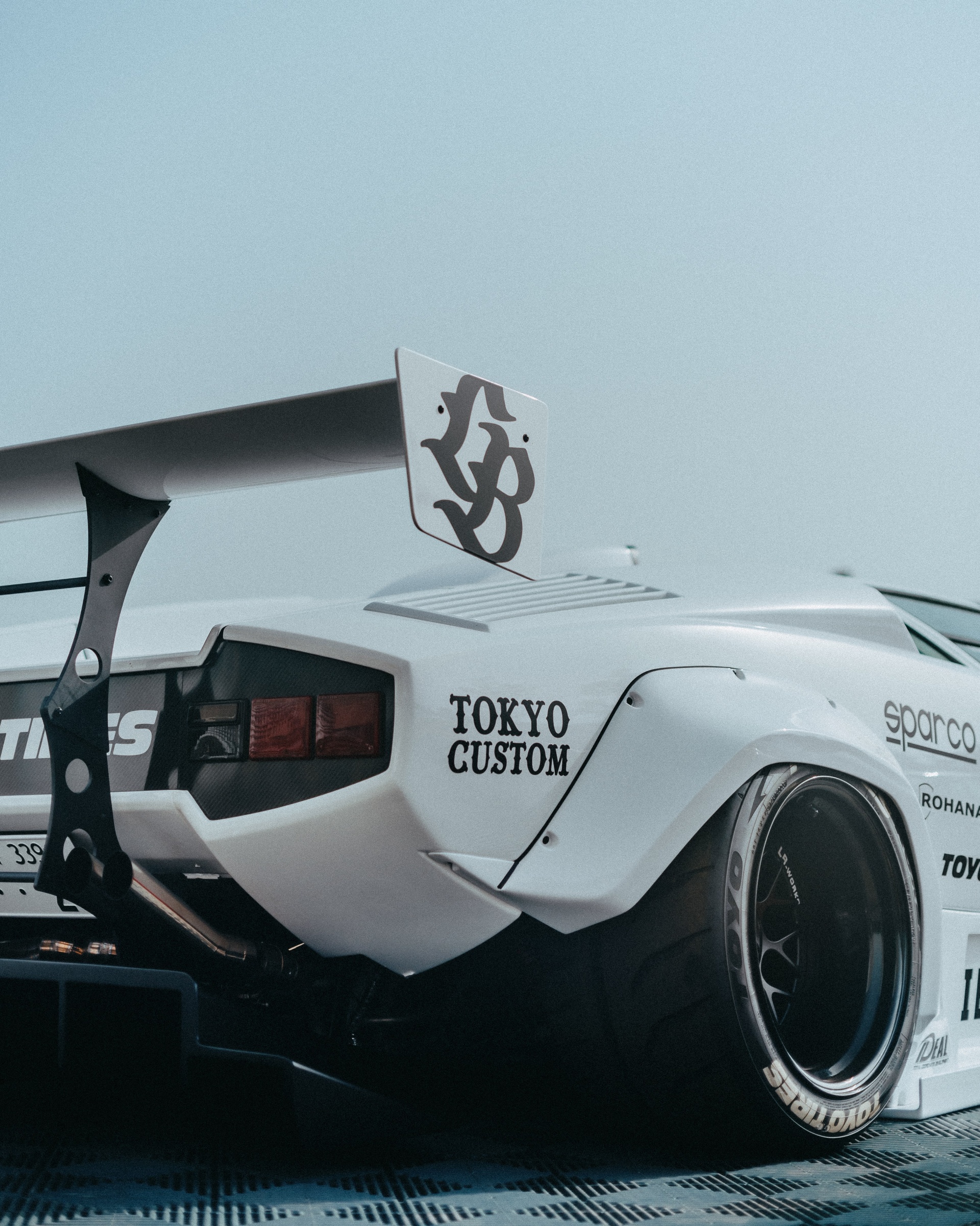 Tylna część białego samochodu tuningowego z oznaczeniem Tokyo Custom i oponami Toyo Tires.