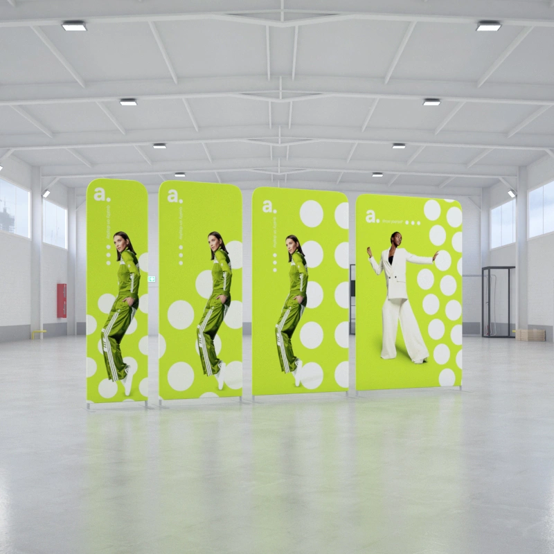 Systemy ścianek tekstylnych z grafiką reklamową ustawione w przestronnej hali, prezentujące modowe wizualizacje na jaskrawym, zielonym tle z białymi kropkami.