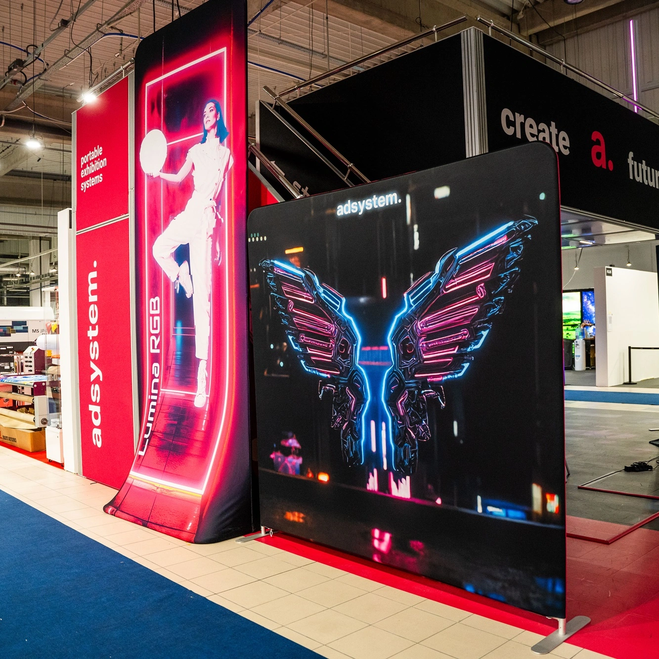 Na zdjęciu widoczne są ścianki reklamowe adsystem z grafikami w stylu neonowym, ustawione na stoisku targowym z hasłem „create a future”.