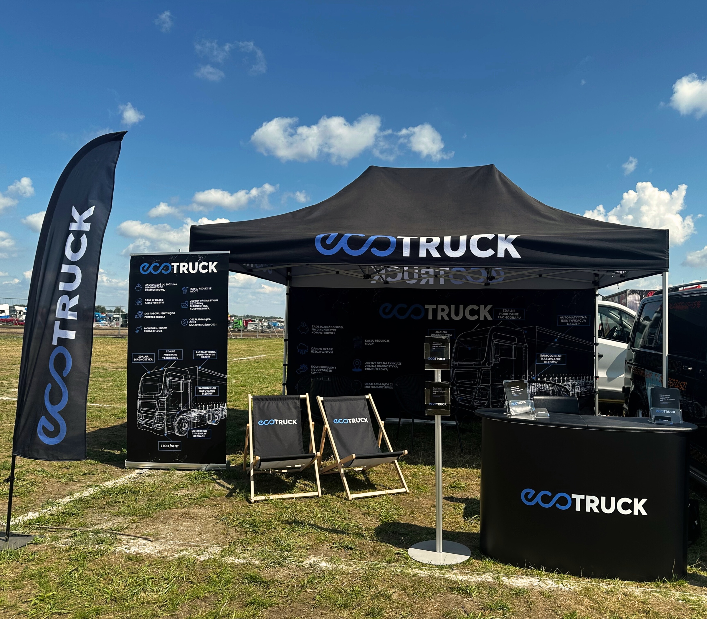file-meta-description.stoiskosponsorskie-eco-trucknawydarzeniuplenerowym–namiotznadrukiem,flagireklamowe,trybunka,leżakiiroll-upzgrafikątechnicznąciężarówki,ustawionenaotwartymtereniepodniebieskimniebem.