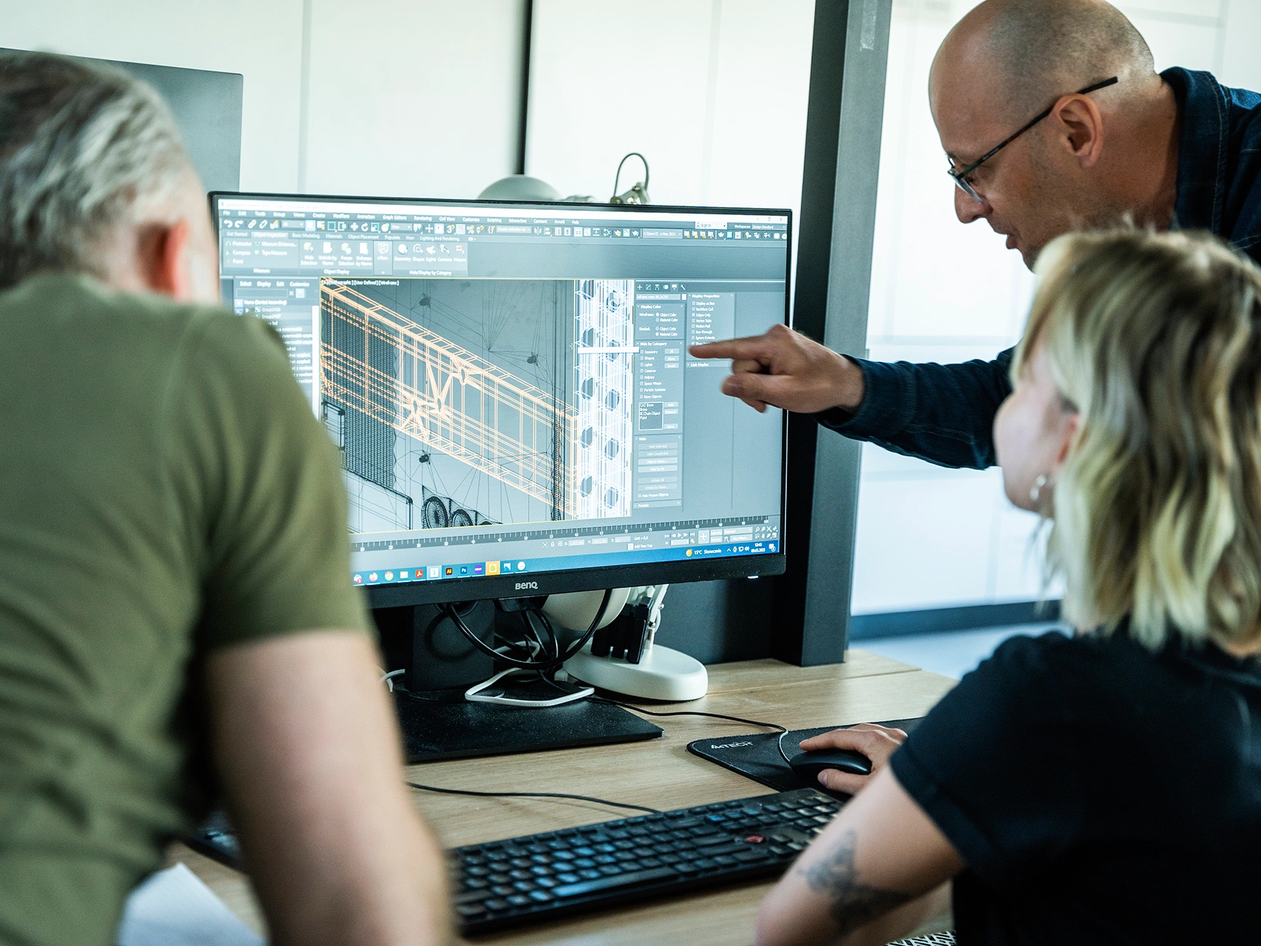 Grupa osób pracuje przy komputerze nad projektem 3D, analizując szczegóły konstrukcji wyświetlane na monitorze.