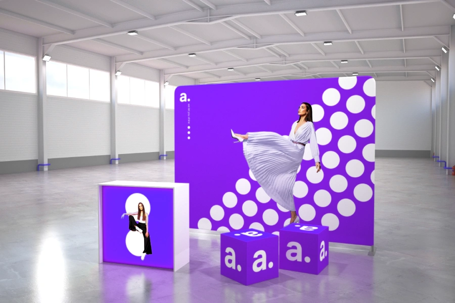 Systemy wystawiennicze w hali – ścianka tekstylna, trybunka i kostki reklamowe w kolorze fioletowym z białymi kropkami i wizerunkiem kobiety.