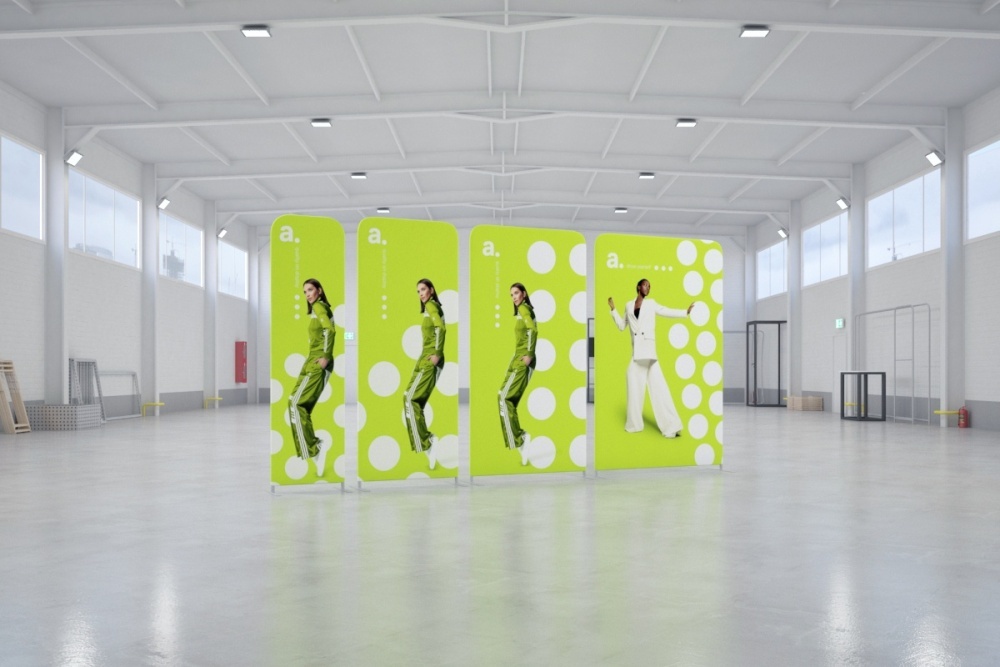 Photocall publicitario en feria montado en un amplio pabellón, con paneles verdes decorados con imágenes de modelos, pensado para atraer miradas y servir como fondo para fotos.