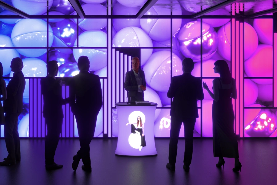 Strefa eventowa z podświetlaną trybunką i ścianą ledową w fioletowo-różowej kolorystyce, wokół której rozmawiają uczestnicy targów.