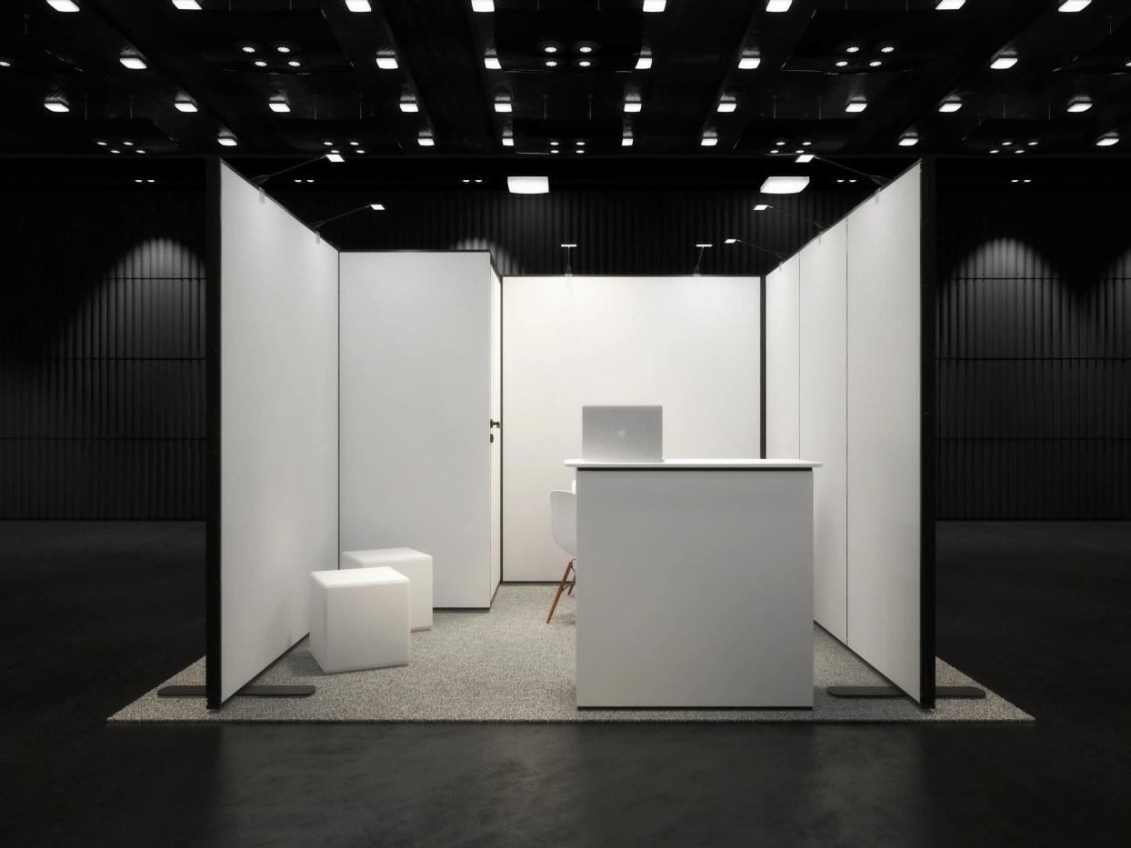 Mock-up stoiska targowego z białymi ściankami, ladą i minimalistycznymi meblami w nowoczesnej hali wystawienniczej.