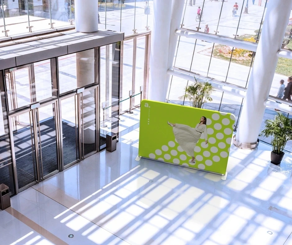 Estructura de aluminio para photocall instalada en la entrada de un edificio luminoso, con gráfico colorido y diseño moderno que invita a tomarse fotos.