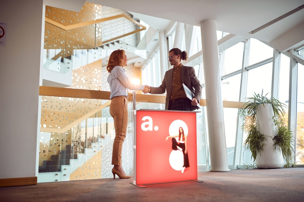 Dwie osoby ściskające dłonie za trybunką reklamową