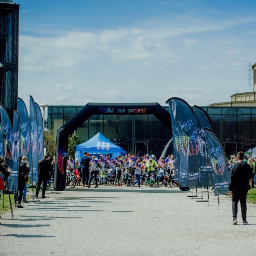 file-meta-description.outdoorsportseventwithbrandedadvertisingflags,aninflatablearch,andabluepromotionaltent,withparticipantsgatheringatthestartingzone.