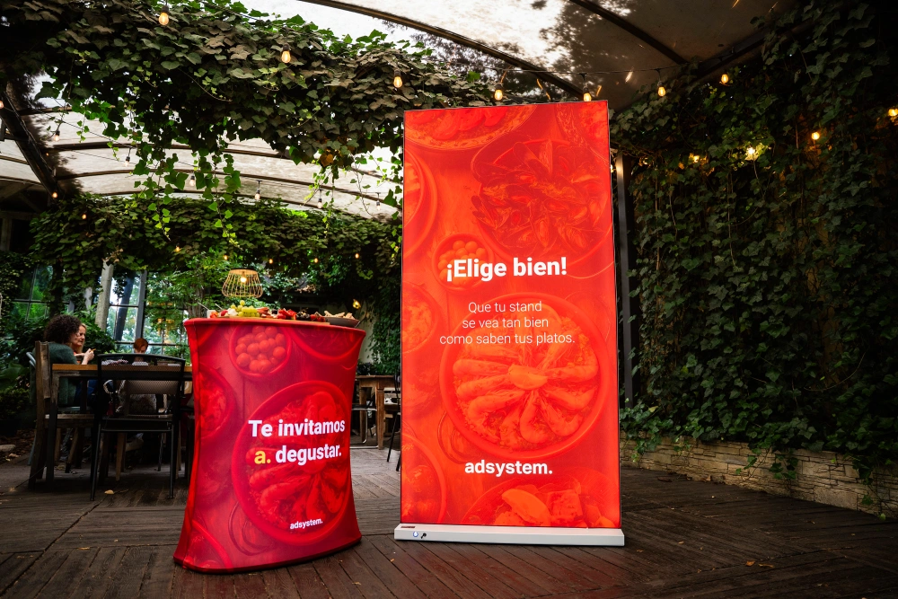 Trybunka i ścianka reklamowa adsystem w czerwonej oprawie z hiszpańskimi hasłami promocyjnymi, ustawione w zielonej, ogrodowej przestrzeni eventowej.