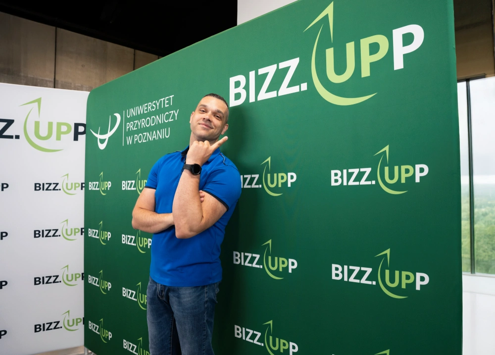 Photocall textil recto para eventos corporativos con fondo verde personalizado de BIZZ.UPP y participante posando frente al logotipo.