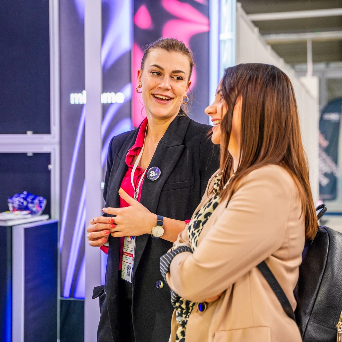 Dwie kobiety rozmawiają z uśmiechem przy stoisku targowym, tworząc atmosferę otwartości i zaangażowania w kontakcie z odwiedzającymi.