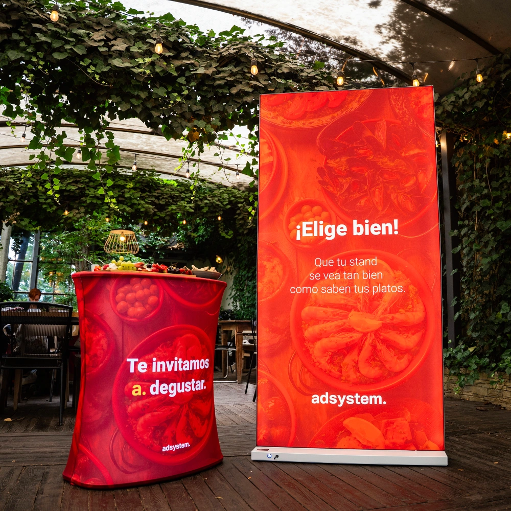 Trybunka i ścianka reklamowa adsystem w intensywnie czerwonej kolorystyce z hiszpańskimi hasłami, ustawione w ogrodowej przestrzeni pod zadaszeniem i girlandami świetlnymi.