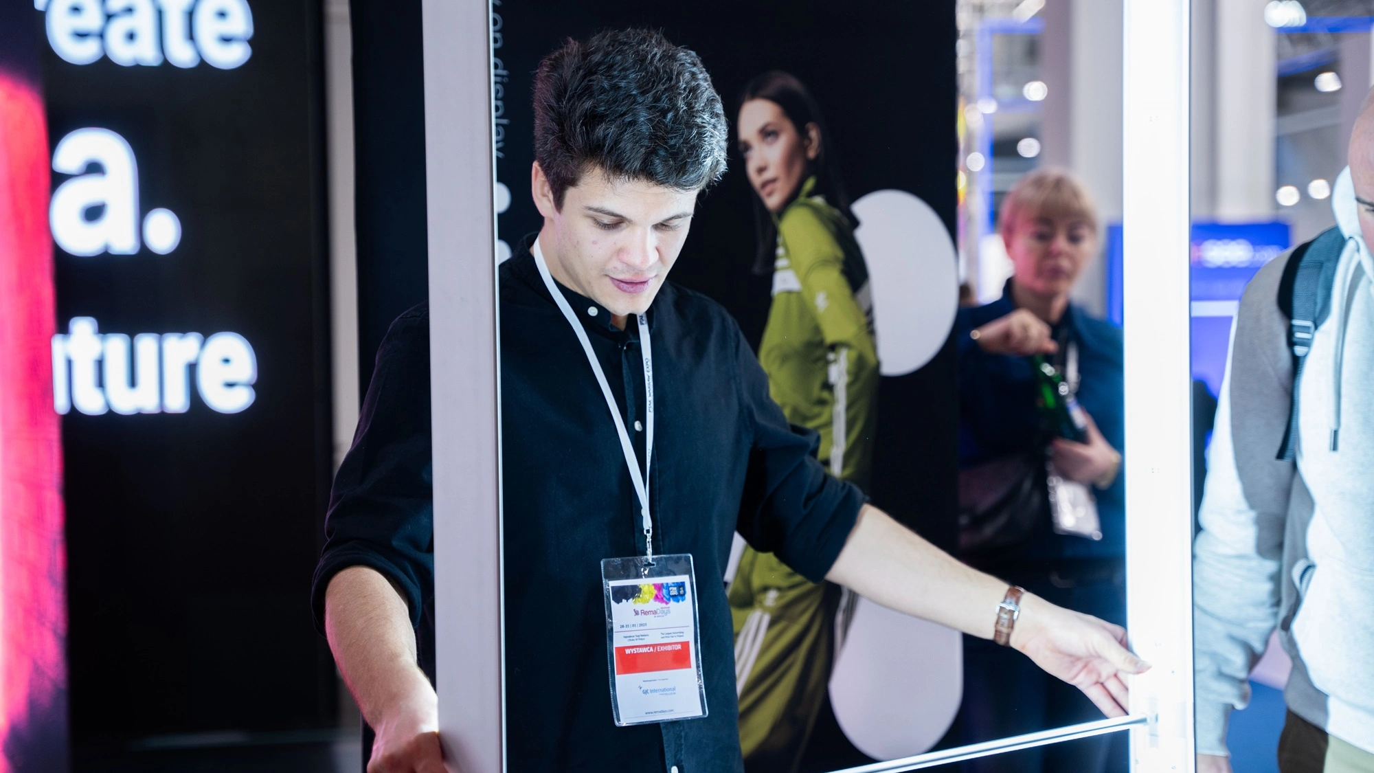 Mężczyzna prezentuje montaż kasetonu tekstylnego z podświetleniem LED podczas targów, na stoisku z systemami wystawienniczymi adsystem.