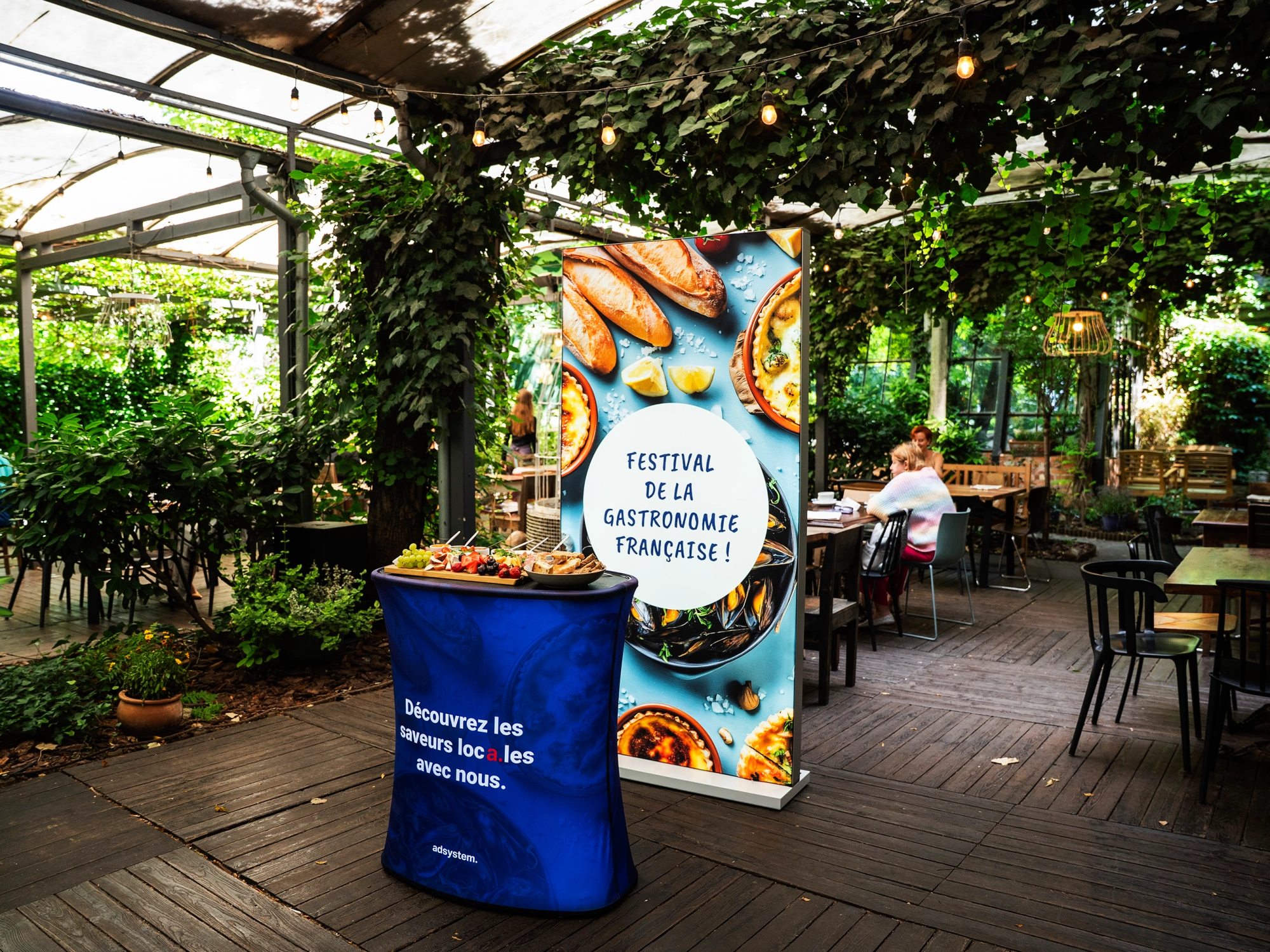 Kaseton reklamowy LED i trybunka promujące „Festival de la Gastronomie Française” w ogrodzie restauracyjnym.