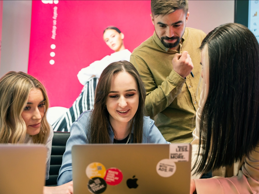 Zespół pracujący przy laptopach omawia szczegóły zamówienia – ilustracja procesu zakupowego krok po kroku.