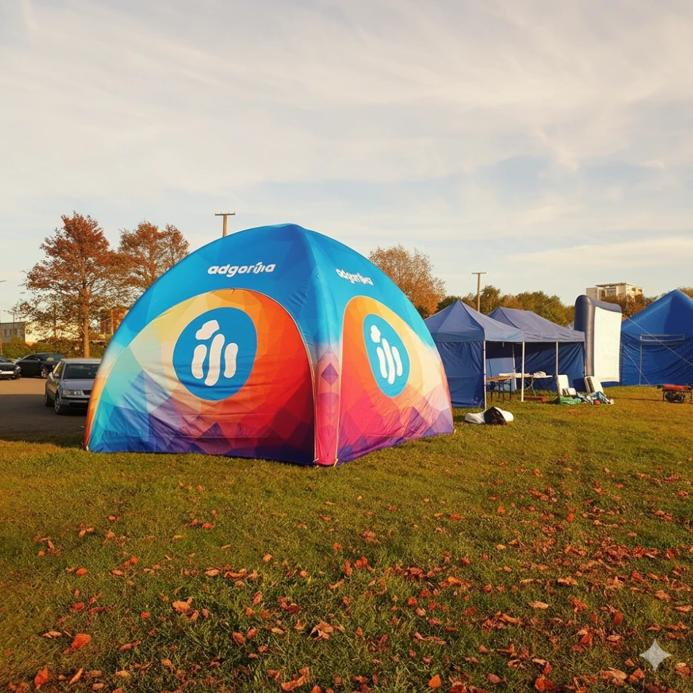 Namiot reklamowy adsystem ustawiony na jesiennej trawie podczas wydarzenia plenerowego, z kolorową grafiką i innymi stoiskami w tle