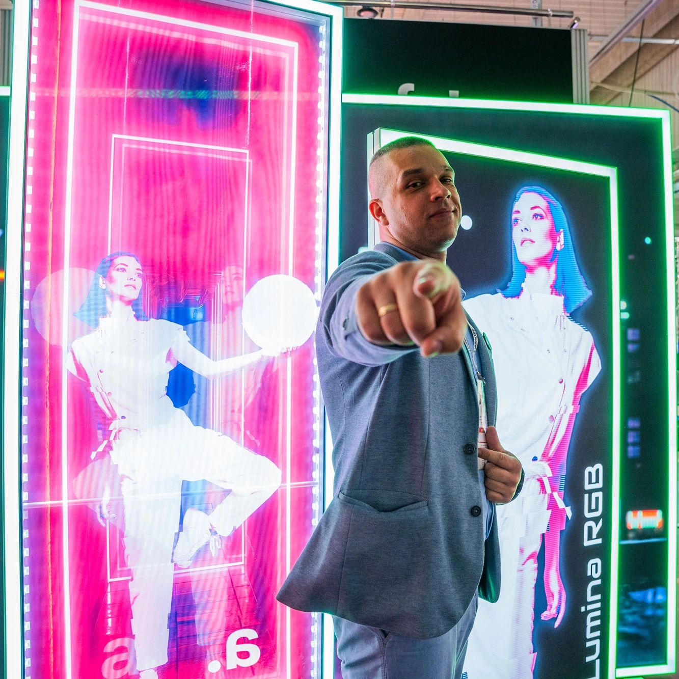 Osoba stojąca przed podświetlanymi kasetonami Lumina RGB na stoisku targowym adsystem, wskazująca w stronę obiektywu.