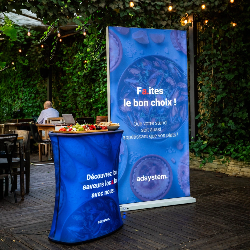 Kaseton podświetlany LED z hasłem „Faites le bon choix !” obok trybunki reklamowej z poczęstunkiem w ogrodzie restauracyjnym.
