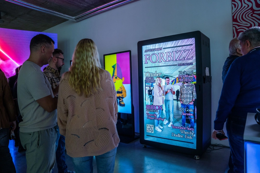 Ludzie oglądający podświetlany infokiosk prezentujący cyfrową okładkę magazynu podczas wydarzenia.