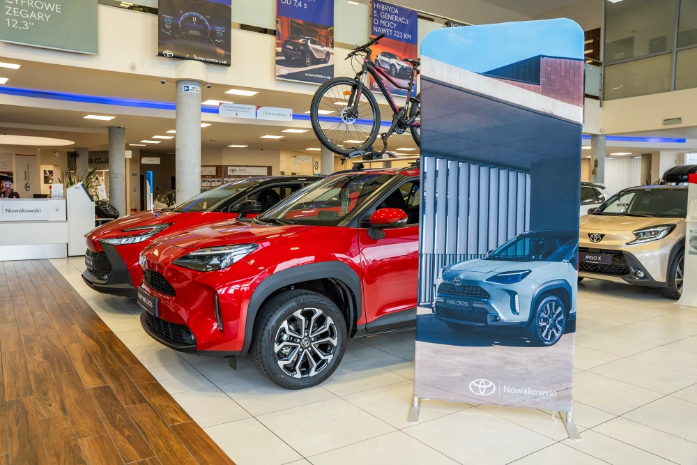 Photocall textil publicitario para ferias con estructura modular de aluminio, colocado en un concesionario Toyota junto a automóviles de exhibición.