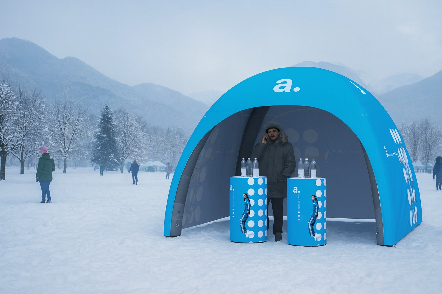 Zimowa strefa eventowa adsystem z niebieskim namiotem pneumatycznym i trybunkami reklamowymi na ośnieżonym tle gór i drzew.