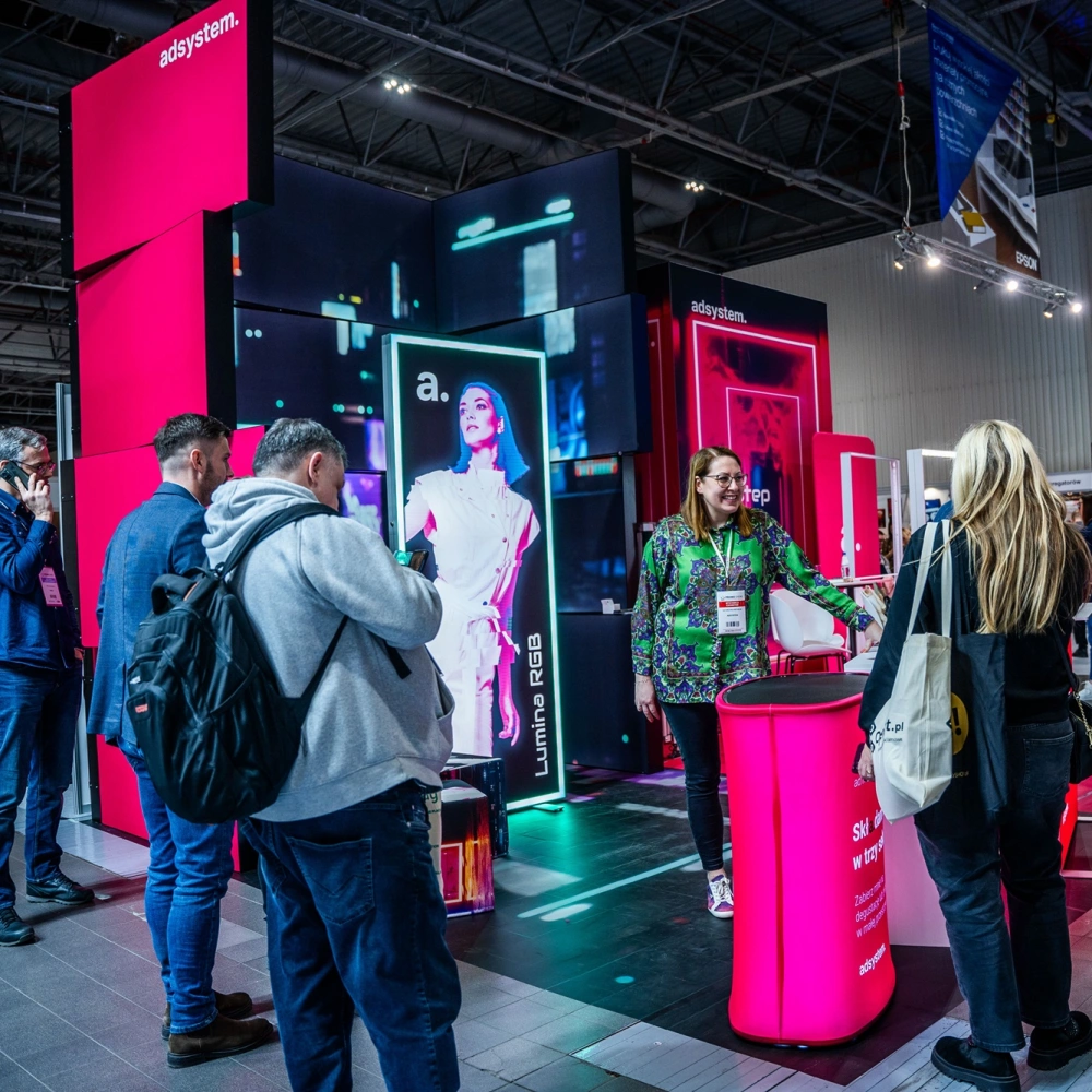 Stand de adsystem en una feria, con pantallas LED Lumina RGB y mobiliario retroiluminado que atraen la atención de los visitantes.