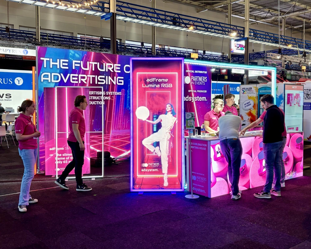 Prezentacja systemów wystawienniczych na stoisku targowym adsystem – rozmowy z odwiedzającymi i przyciągająca wzrok oprawa świetlna.
