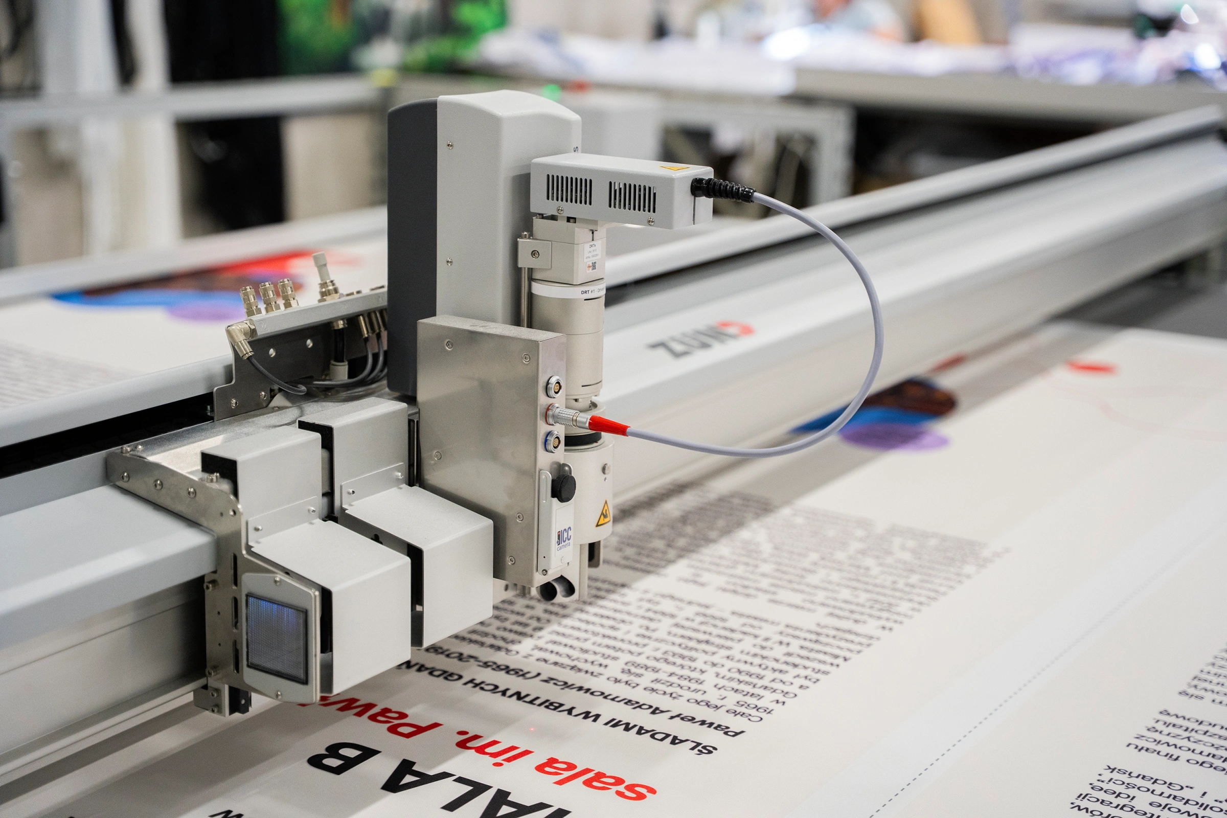 Zbliżenie na głowicę plotera ZUND w trakcie precyzyjnego cięcia grafiki z oznaczonymi liniami i markerami.